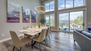 A dining area with a large table set for six, surrounded by chairs, with artwork on the walls and a view of the outdoors through large windows. - Fairmont Peak Cabin | Pet Friendly | Pool Table (Area F (Columbia Lake/Windermere Lake))