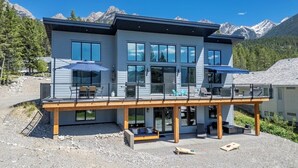 A modern two-story house with a balcony, large windows, and a view of mountains. - Fairmont Peak Cabin | Pet Friendly | Pool Table (Area F (Columbia Lake/Windermere Lake))
