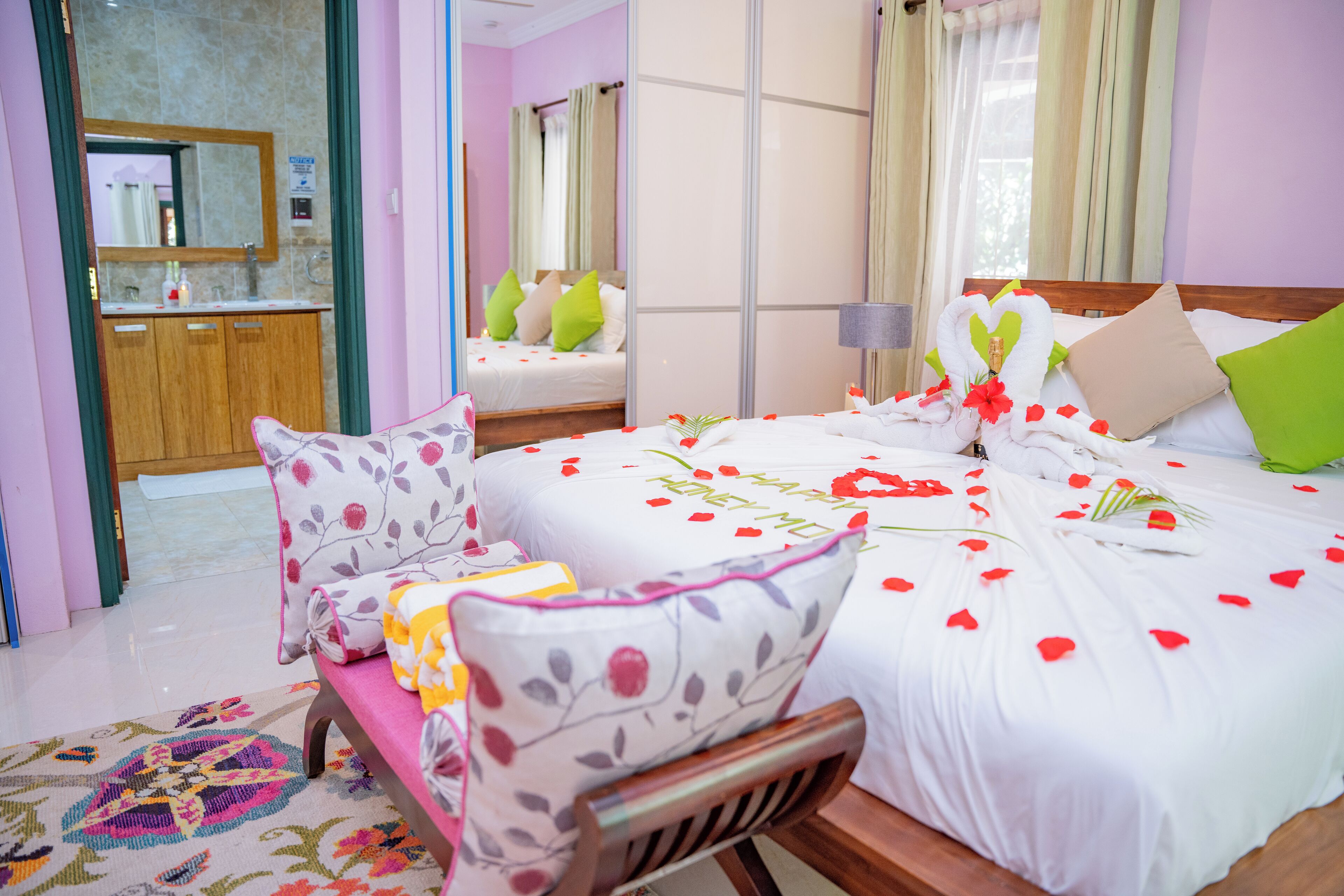 Ein Hotelzimmer mit Bett, einer Bank, einem Spiegel und einem durchgegangenen Tür einsehbaren Badezimmer.