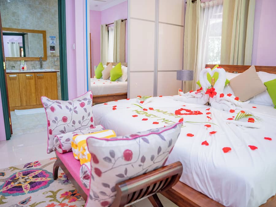 Ein Hotelzimmer mit Bett, einer Bank, einem Spiegel und einem durchgegangenen Tür einsehbaren Badezimmer.