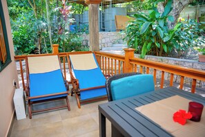 A covered outdoor seating area with two wooden lounge chairs and a table, surrounded by lush greenery and a stone wall. - Pension Michel - Villa Roche Bois (La Digue)