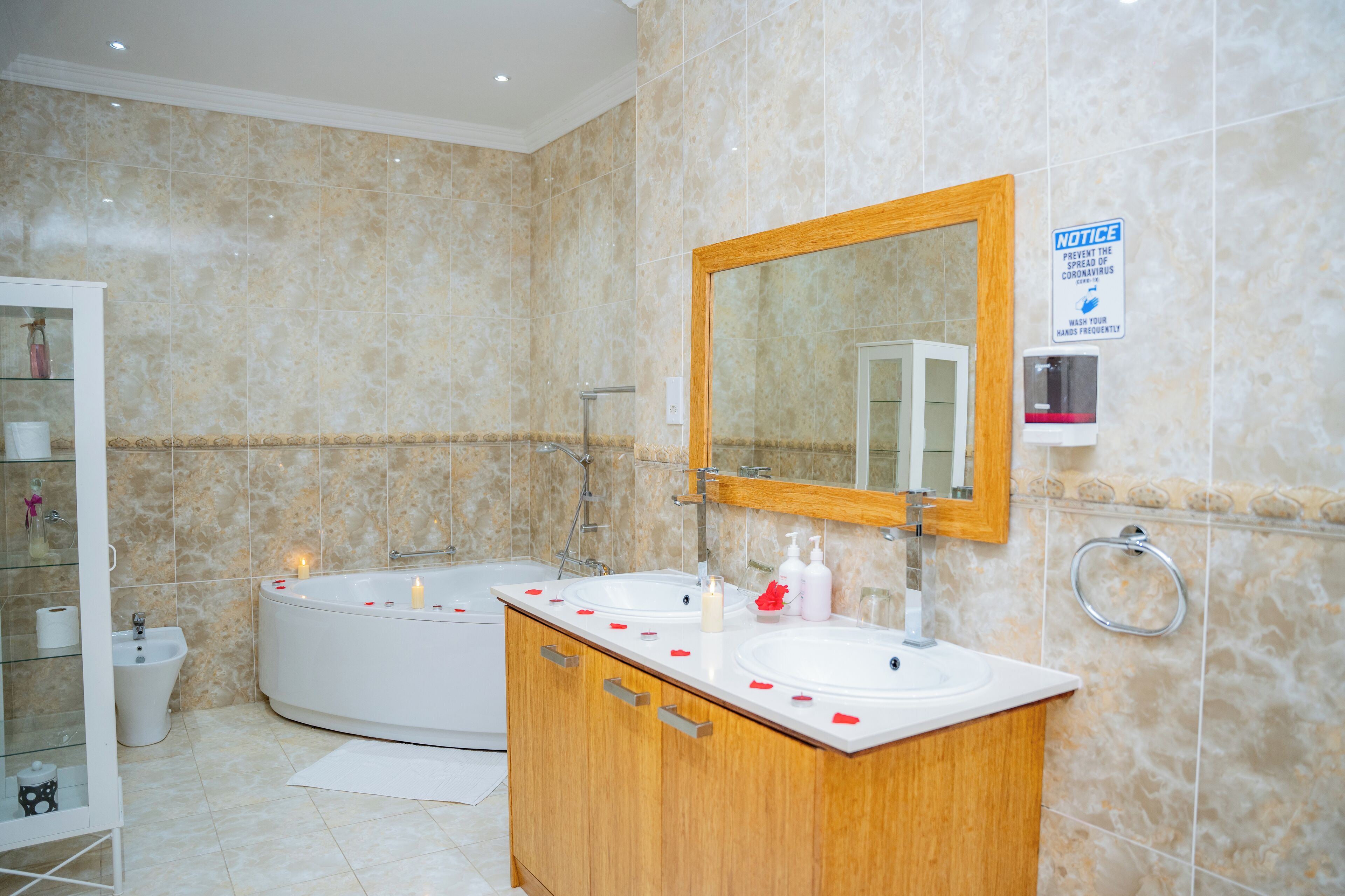 Une salle de bain moderne dotée d’un grand miroir, de deux lavabos, d’une baignoire et d’un distributeur de gel hydroalcoolique.