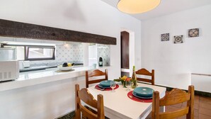 Una cucina compatta con zona pranzo, caratterizzata da un piano di lavoro bianco, sedie in legno e un lampadario.