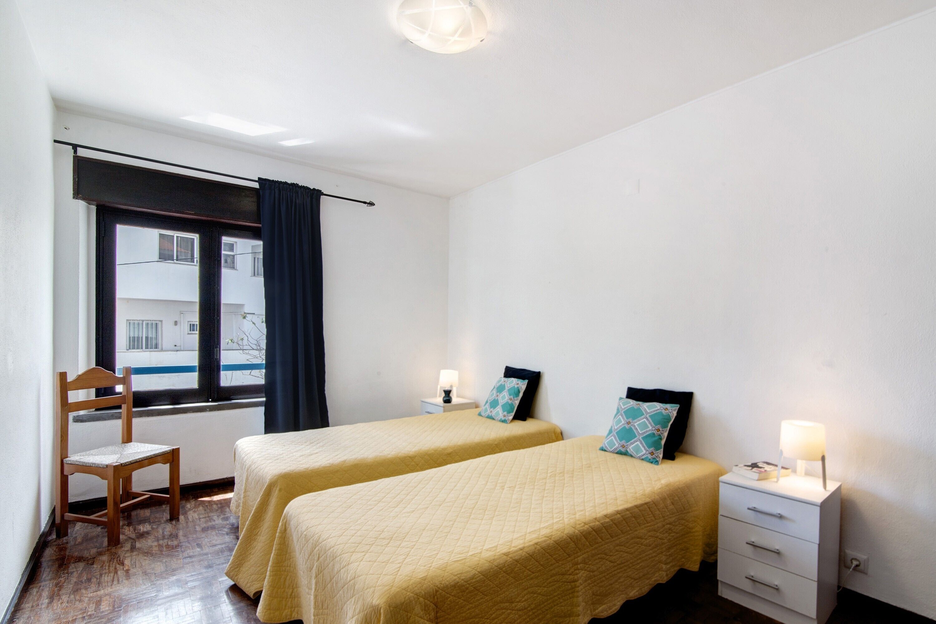 A room with two beds, a chair, a nightstand, and a window with a view of buildings.