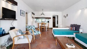 Una stanza compatta con un letto, un divano, un tavolo da pranzo con sedie, una TV a parete e una piccola cucina in secondo piano.