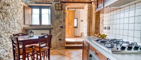 Una cocina rústica con paredes de ladrillo visto, una mesa de madera con sillas, una estufa a gas y un salpicadero de azulejos.