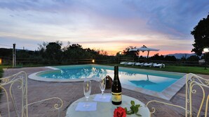 A poolside setting with a sunset view, a bottle of wine, a glass, and a rose on a table. - Holiday Home 'Casale Storico XVII Sec - Rosa' with Mountain View, Shared Pool and Wi-Fi (Giano dell'Umbria)