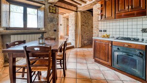 A rustic kitchen with exposed brick walls, wooden cabinets, a dining table with chairs, and a built-in oven. - Holiday Home 'Casale Storico XVII Sec - Rosa' with Mountain View, Shared Pool and Wi-Fi (Giano dell'Umbria)