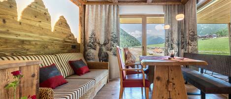 A wooden interior with a sofa, bench, and dining table, large windows with a mountain view.