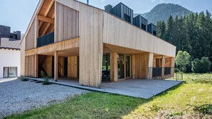 Ein modernes Holzhaus mit einer großen Terrasse, einer Treppe und Blick auf einen bewaldeten Berg.