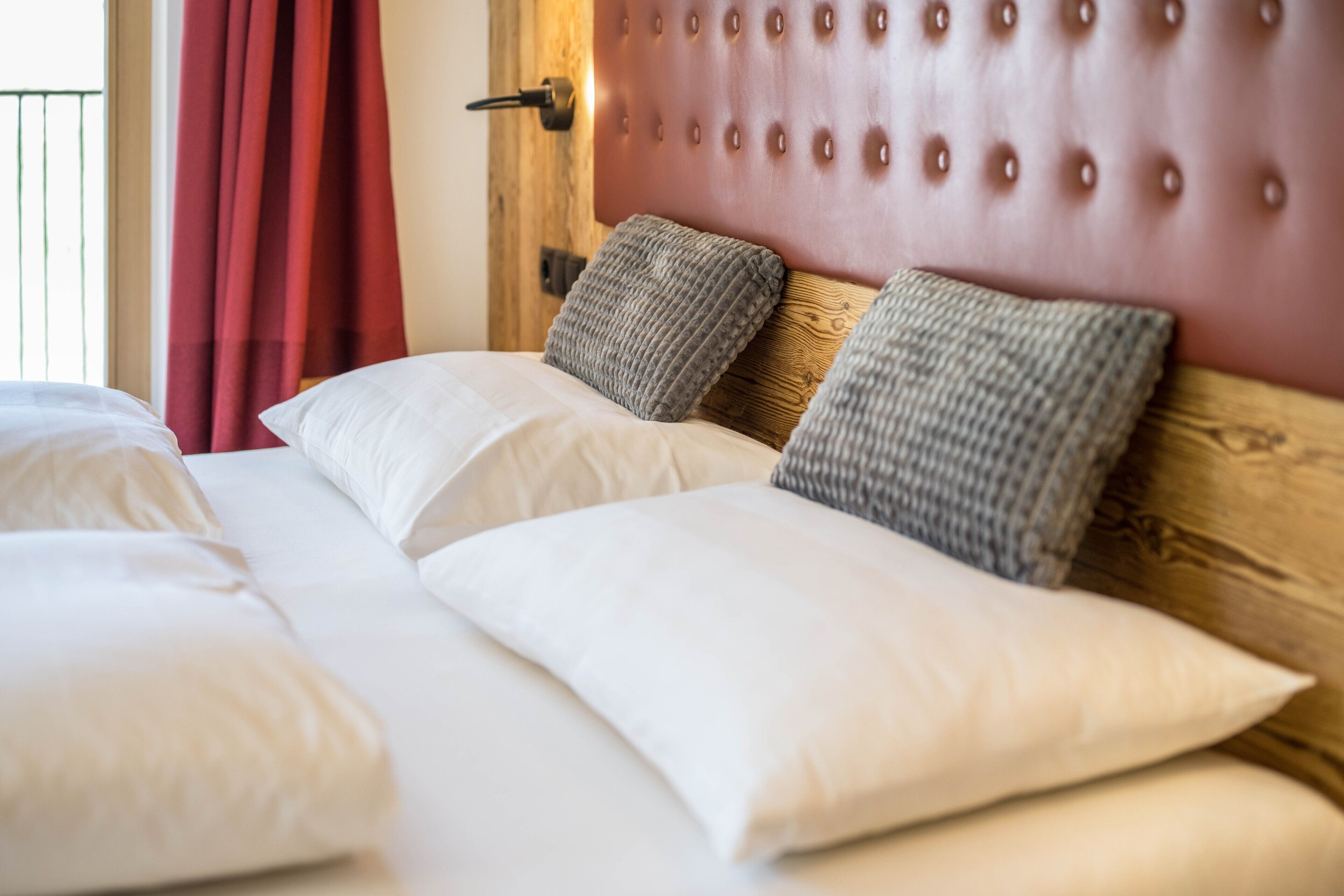 A bed with white and grey pillows, a wooden headboard, and a red curtain.
