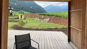 Une terrasse en bois avec une chaise, une vue sur un paysage montagneux et un bâtiment doté d’un balcon.