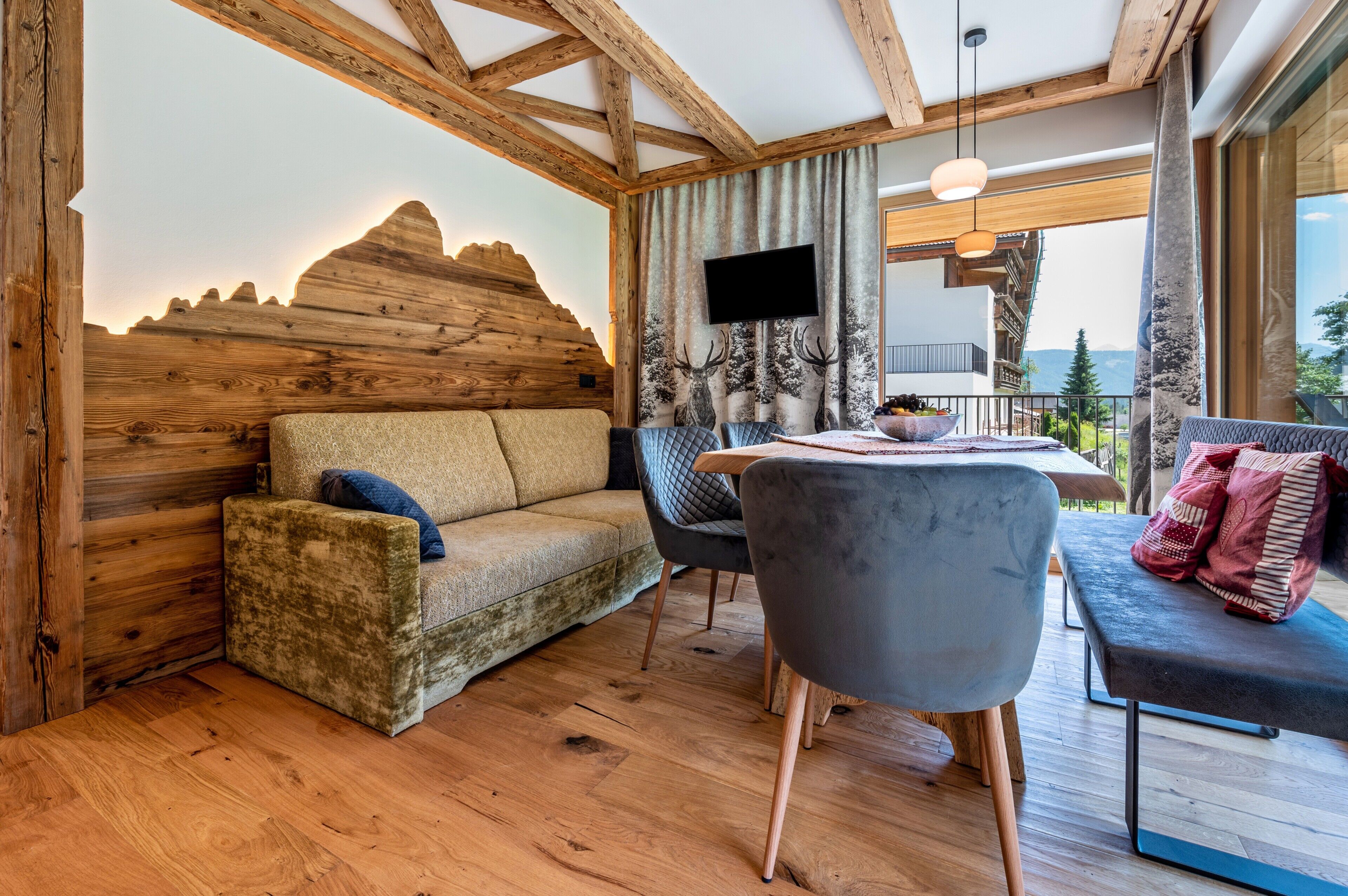 Una habitación acogedora con techo de madera, un sofá, una silla, una mesa con un tazón y un televisor en la pared.