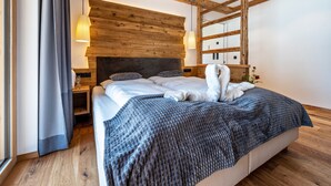 Une chambre à coucher moderne avec une tête de lit en bois, un grand lit recouvert d’une couverture à motifs, une table de chevet avec une lampe et une fenêtre avec des rideaux.