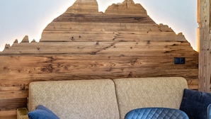 Un mur en bois orné d’un motif de montagne, un canapé avec des coussins et un petit panneau de commande.