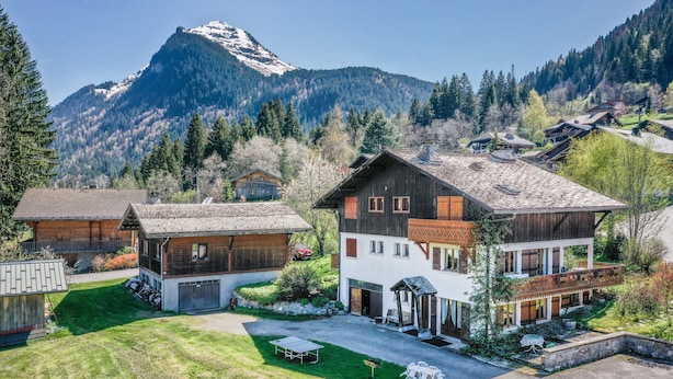 Un chalet de montagne doté d’une grande terrasse, de bâtiments en bois et offrant une vue sur des montagnes enneigées.