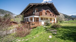 Un chalet en bois doté d’un balcon, entouré de verdure et de montagnes.