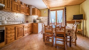 Une cuisine avec des meubles en bois, une table à manger avec des chaises, un four à micro-ondes et un téléviseur.