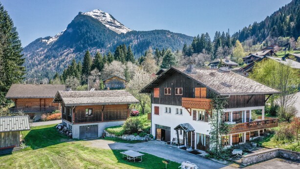Un chalet de montagne doté d’une grande terrasse, de bâtiments en bois et offrant une vue sur des montagnes enneigées.