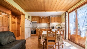 Une cuisine chaleureuse avec des meubles en bois, une table à manger avec des chaises, un canapé et une grande fenêtre avec des rideaux.