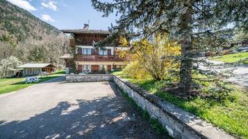 Un bâtiment à deux étages, doté de fondations en pierre, d’une allée pavée et d’un espace verdoyant avec des arbres.