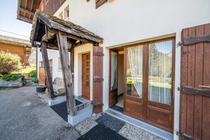 Un edificio tradicional de madera con una escalera de madera que lleva a una puerta, un pequeño porche y una ventana con cortinas.
