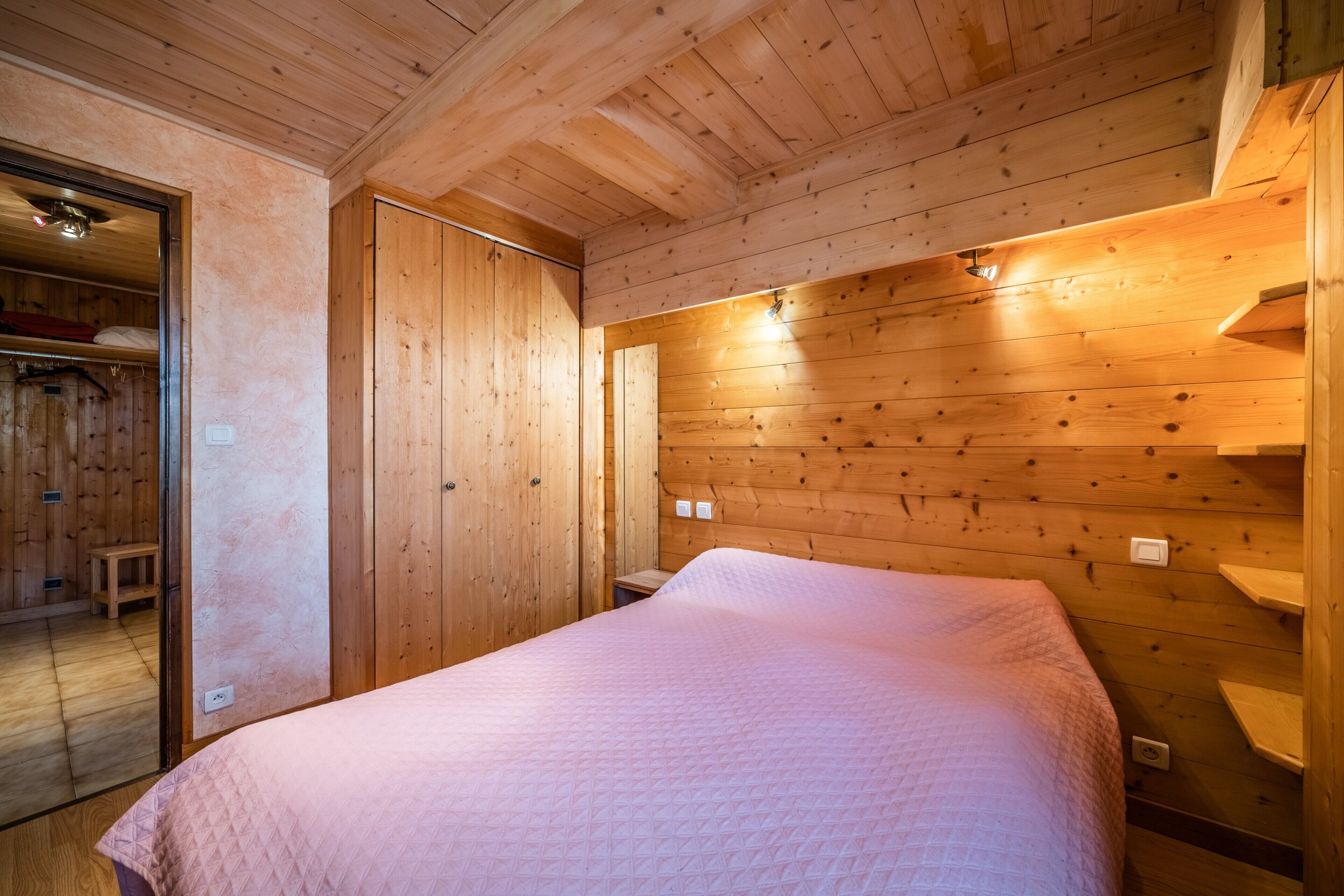 A wooden-paneled room with a bed, a bench, and a door leading to another room.