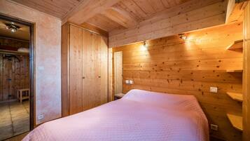 A wooden-paneled room with a bed, a bench, and a door leading to another room.