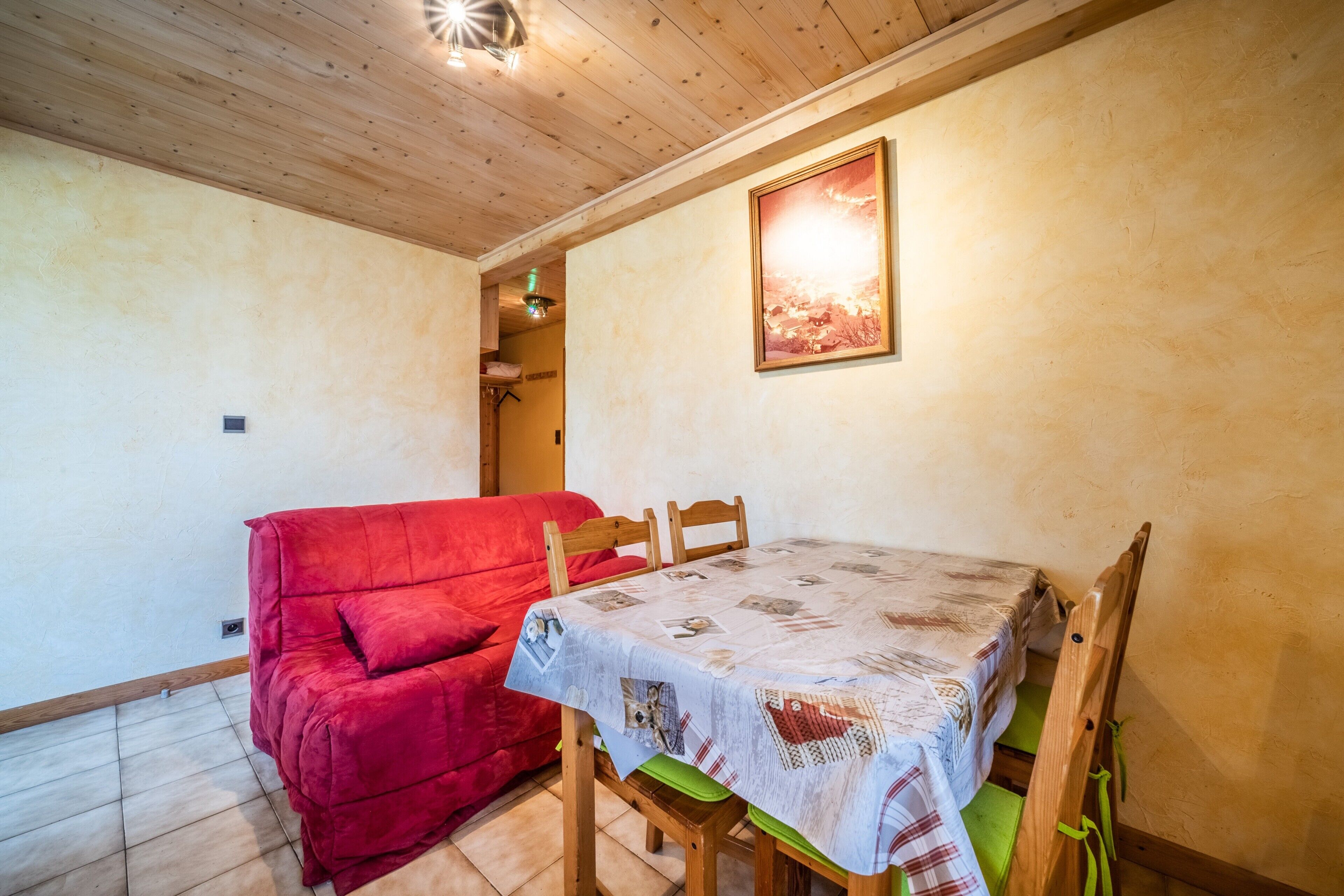 Un coin repas avec une table dressée pour quatre personnes, un canapé rouge, des chaises en bois et un tableau encadré au mur.