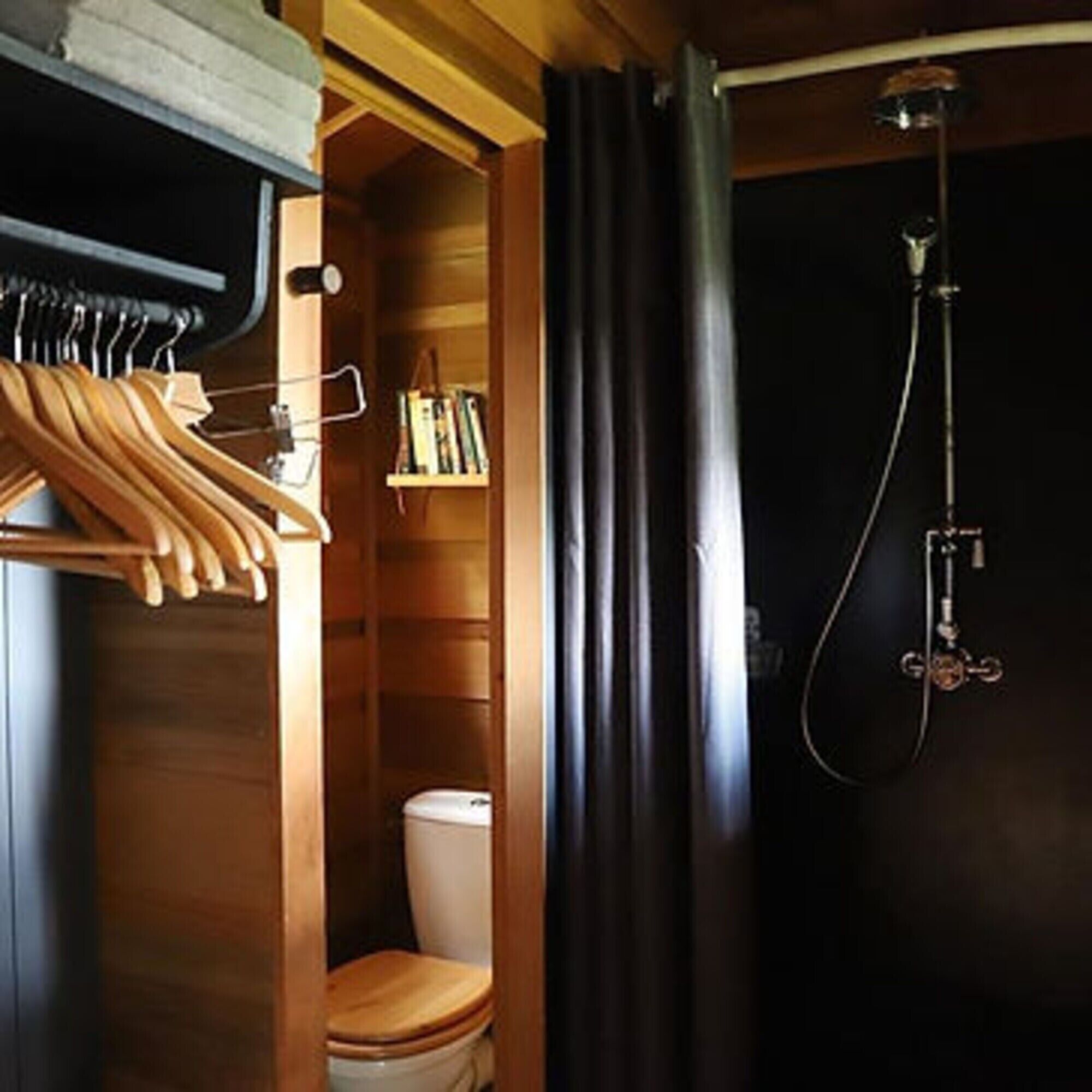 Un intérieur en bois avec des toilettes en bois, une douche avec un rideau et une étagère en bois remplie de livres.