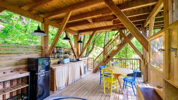 Eine Holzterrasse mit Esstisch, Stühlen, einem Kühlschrank und hängenden Pendelleuchten.