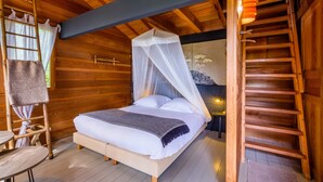 Un dormitorio de cabaña de madera con cama, una escalera, una silla y una mesita.