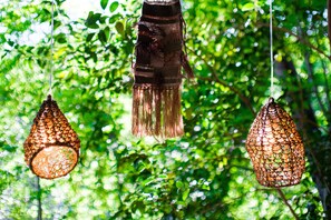 Des lampes suspendues à la structure ajourée, placées sur un fond de feuillage verdoyant.