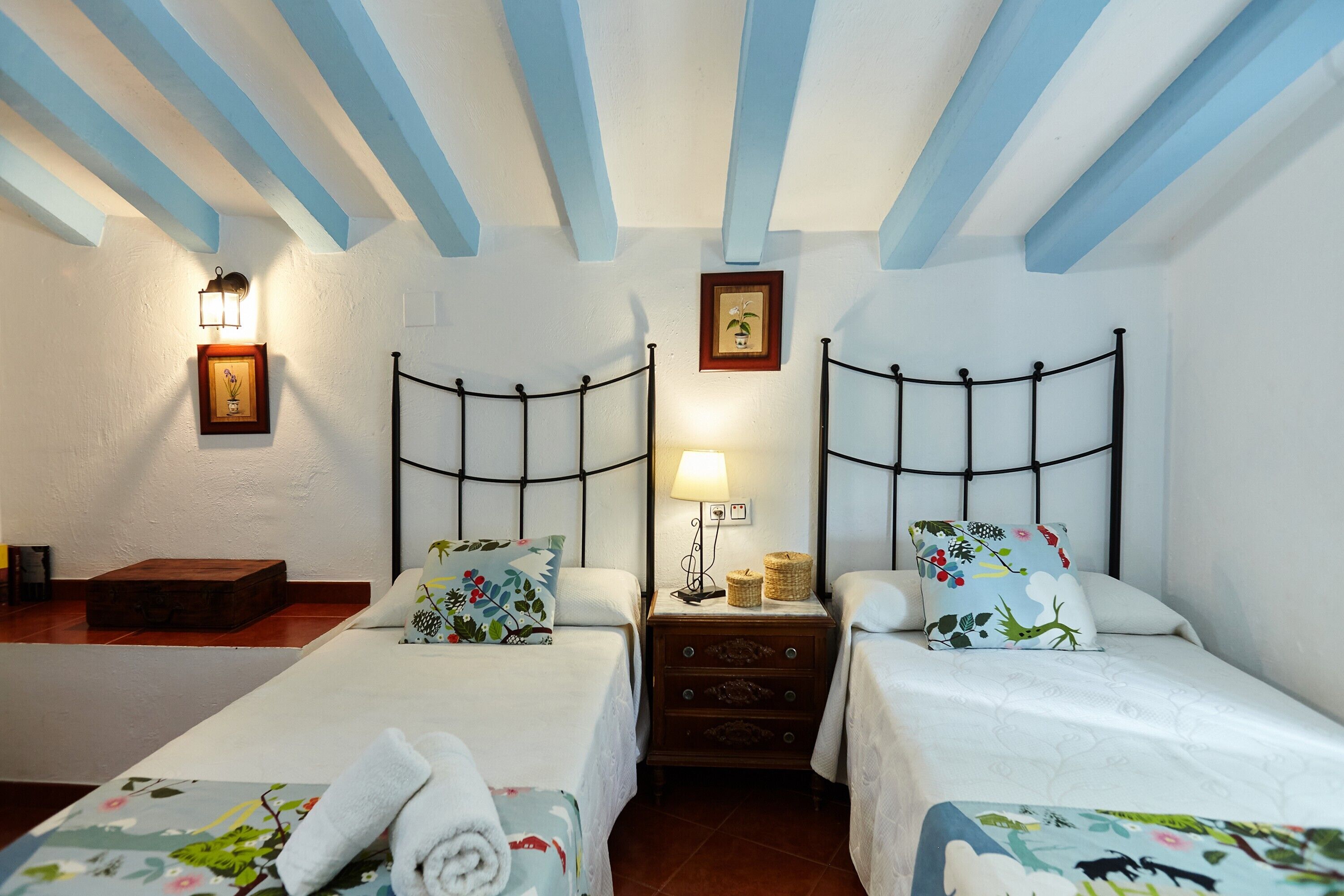 A bedroom with two beds, a nightstand, a lamp, and a framed picture on the wall.