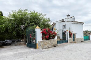 Un bâtiment blanc avec un socle en pierre, un portail en métal et des fleurs rouges devant.
