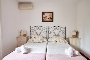 Un lit double avec des coussins à motifs floraux, une table de chevet avec une lampe et un climatiseur fixé au mur.