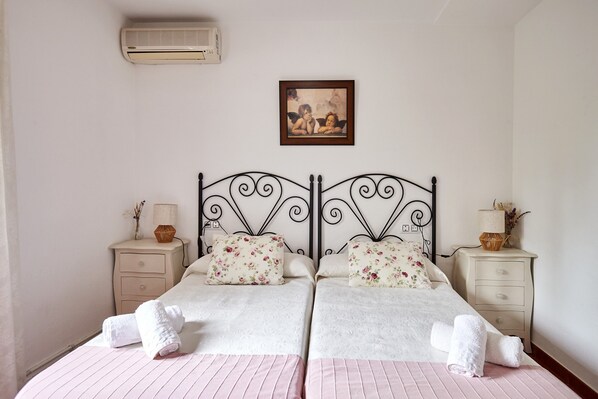 A double bed with floral pillows, a bedside table with a lamp, and a wall-mounted air conditioner.