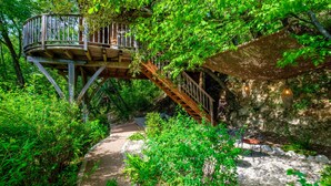 A wooden treehouse with a spiral staircase, surrounded by lush greenery and a stone pathway. - Holiday treehouse "Bagheera" with Shared Pool, Private Terrace & Wi-Fi (Saint-Paul)