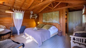 A wooden cabin bedroom with a bed, bedside table, lamp, and a view of the outside. - Holiday treehouse "Bagheera" with Shared Pool, Private Terrace & Wi-Fi (Saint-Paul)