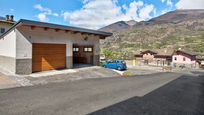 A building with a garage, a blue car parked in front, and a mountainous landscape in the background. - Apartment "Caratteristico e Accogliente" with Mountain View (Pila)