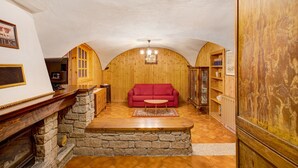 A cozy room with a fireplace, a red sofa, wooden walls, and a stone accent wall. - Apartment "Caratteristico e Accogliente" with Mountain View (Pila)
