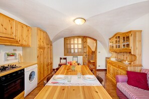 Une cuisine avec des meubles en bois, un lave-linge, une table à manger avec des chaises et un canapé rouge.