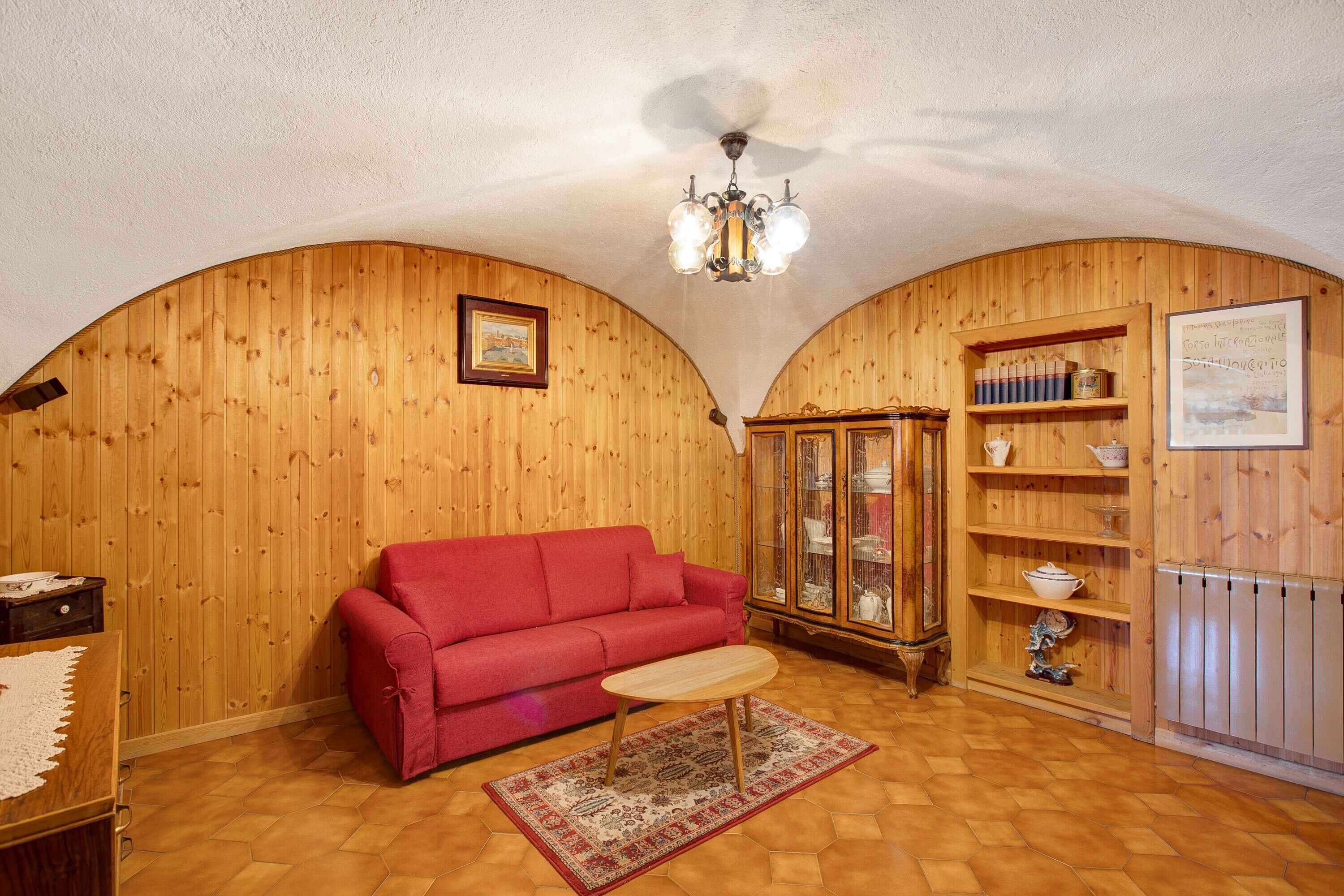 A room with wooden walls, a red sofa, a wooden cabinet, and a chandelier.