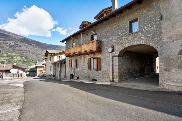 Un bâtiment en pierre doté d’un balcon en bois, un ciel dégagé et une montagne en arrière-plan.