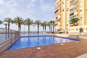 Une piscine dotée d’une terrasse en bois, entourée de palmiers et bordée d’un immeuble de grande hauteur.
