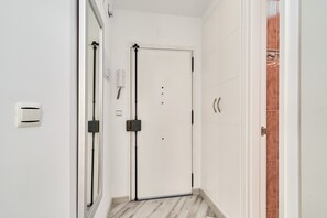 Un couloir avec une porte blanche, un miroir, un détecteur de fumée et un interrupteur fixé au mur.