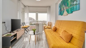 A modern living room with a sofa, a TV, a small table with a plant, and a balcony with a view. - Studio Apartment "Fetén Algarrobo Costa" with Sea View, Private Pool & Wi-Fi (Algarrobo Costa)