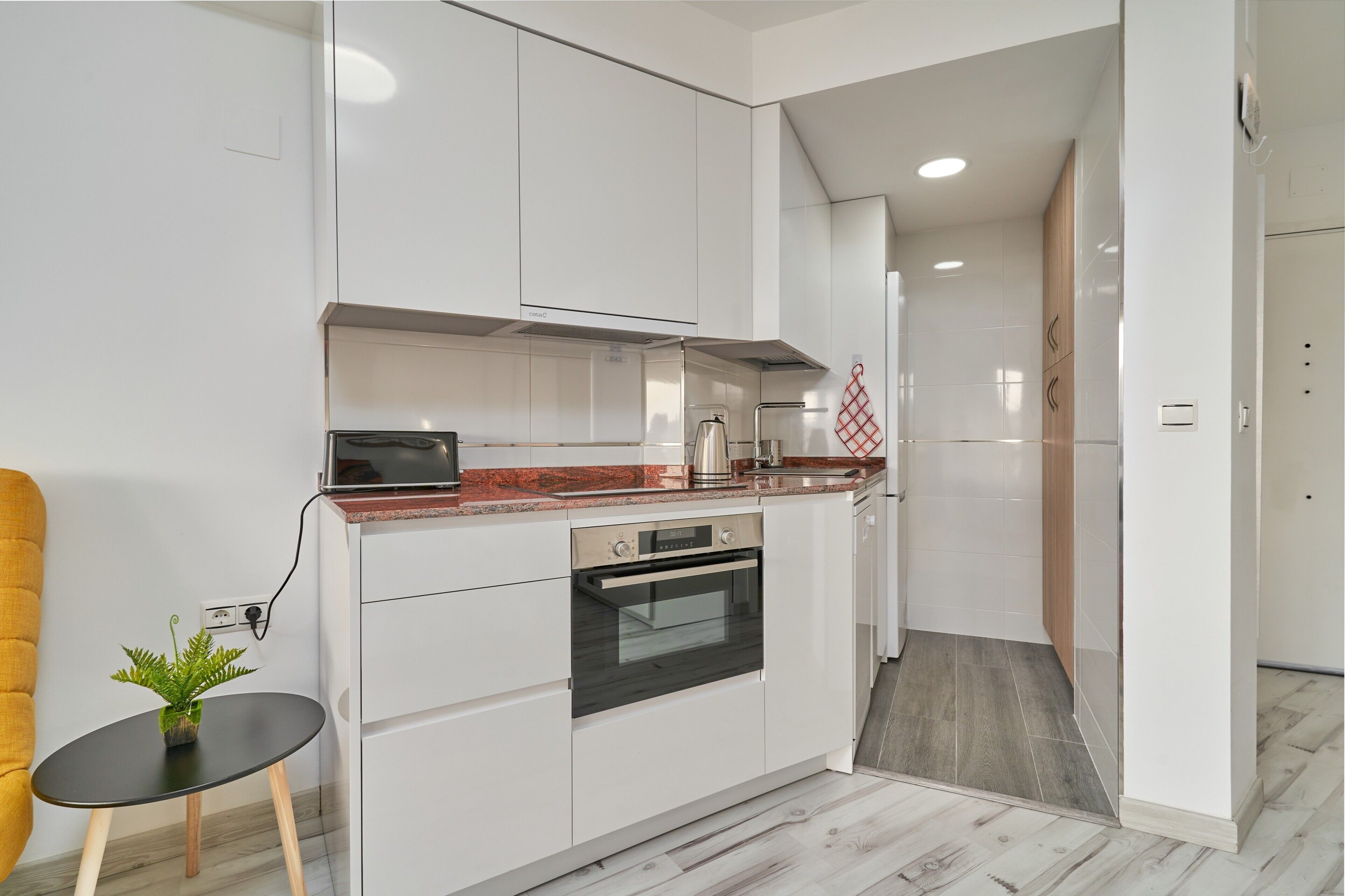 Cocina moderna con armarios blancos, horno empotrado y una pequeña mesa con una planta.