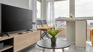 A modern living room with a flat-screen TV, a small round table with a plant, a sofa with a yellow cushion, and a balcony with a view of the city. - Studio Apartment "Fetén Algarrobo Costa" with Sea View, Private Pool & Wi-Fi (Algarrobo Costa)