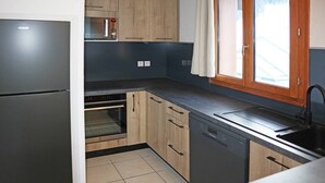 Une cuisine équipée d’un réfrigérateur, d’un four, d’un lave-vaisselle et d’une fenêtre avec des rideaux.